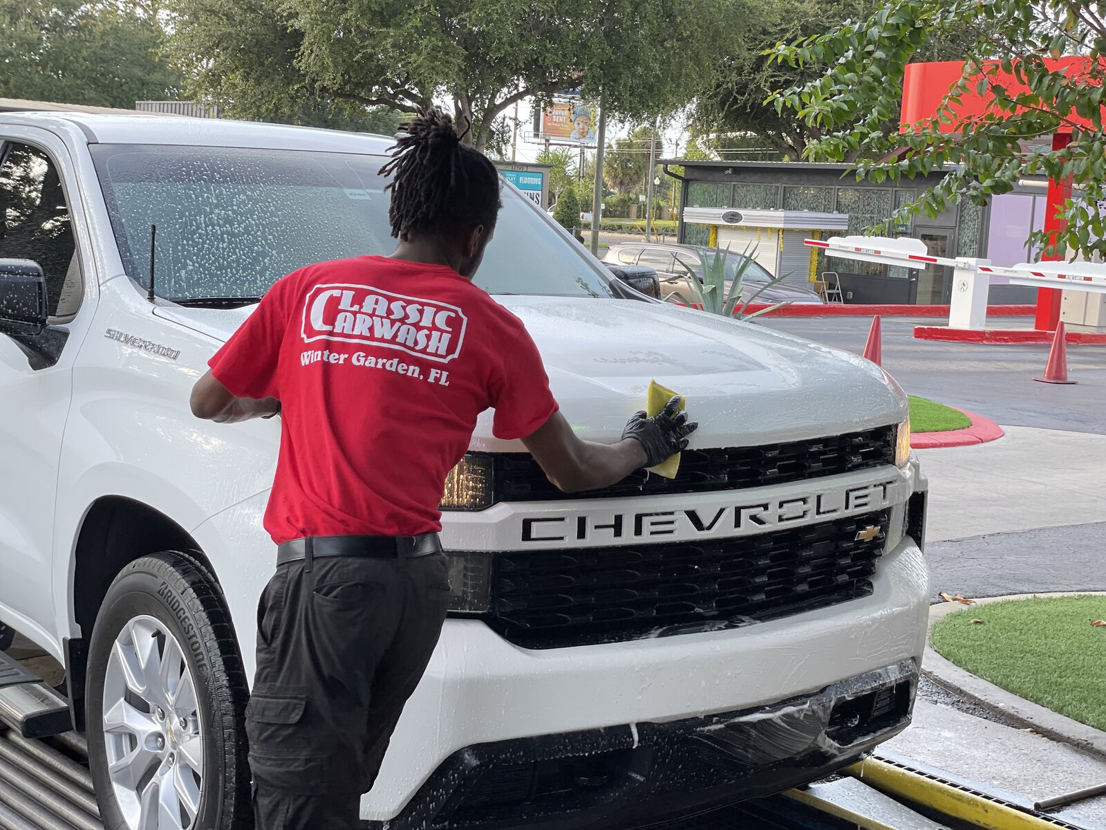 Classic Carwash team member in red Winter Garden, FL uniform hand-washing a white truck